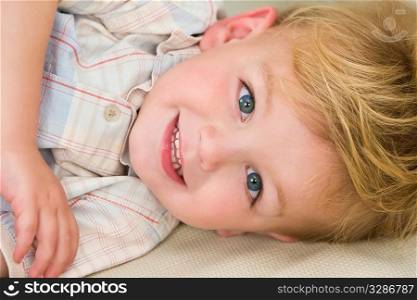 A young blonde boy dressed laying down and giving a cheeky grin