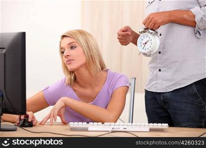 a young blonde woman is doing computer and a man is showing an alarm clock