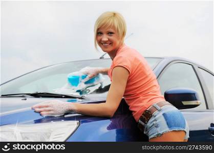 A young blonde woman washes her car