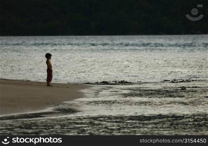 A young boy (6-8) standing on a beach at dusk, Moorea, Tahiti, French Polynesia, South Pacific