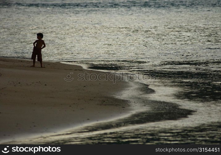 A young boy (6-8) standing on a beach, Moorea, Tahiti, French Polynesia, South Pacific