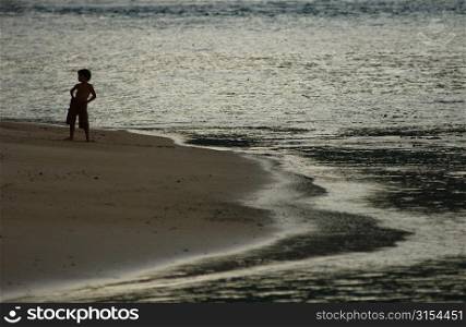 A young boy (6-8) standing on a beach, Moorea, Tahiti, French Polynesia, South Pacific