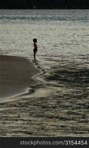 A young boy (6-8) standing on a beach, Moorea, Tahiti, French Polynesia, South Pacific