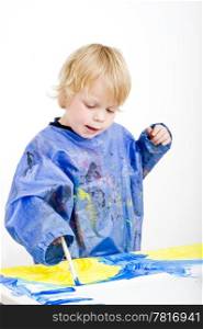 A young boy absorbed with painting with poster paint
