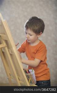 A young boy drawing onto a canvas with a pot of coloured pencils stood on the ledge of the canvas