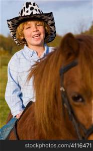 A young boy having fun riding a pony and dressed as a cowboy