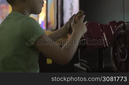 A young boy is playing on game machine in a game zone. He is enthusiastically twisting a wheel and moving other levers. There is some simple body art on the visible part of his face