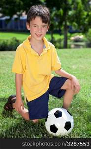 A young boy outside playing soccer or football kneeling on the grass in the shadow of the goal
