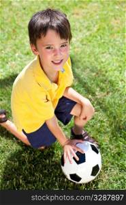 A young boy outside playing soccer or football kneeling on the grass in the shadow of the goal