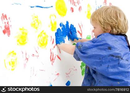 A young boy pressing his hands, covered with blue paint, against a wall, making prints with finger paint