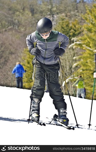 A young boy putting on his snow skis for a day of fun.