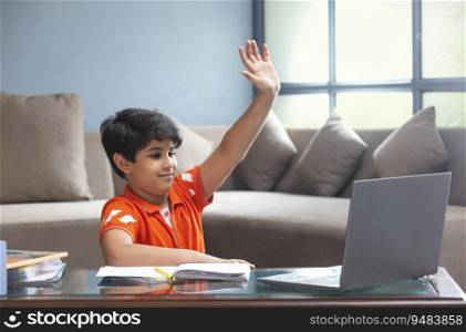 A YOUNG BOY RAISING HAND TO ANSWER DURING ONLINE CLASS
