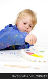 A young boy, reaching to fill his brush with poster paint