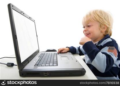 A young boy sits in profile using a laptop computer. He is smiling, viewable from the waist up, and looking away from the camera, at the screen. Horizontally framed shot.