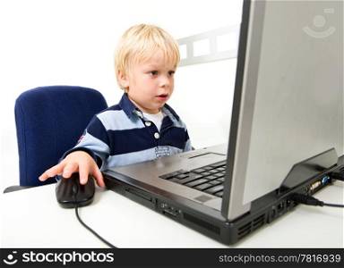 A young boy sits using a laptop computer. He is viewable from the chest up and is looking away from the camera at the laptop screen. Horizontally framed shot.