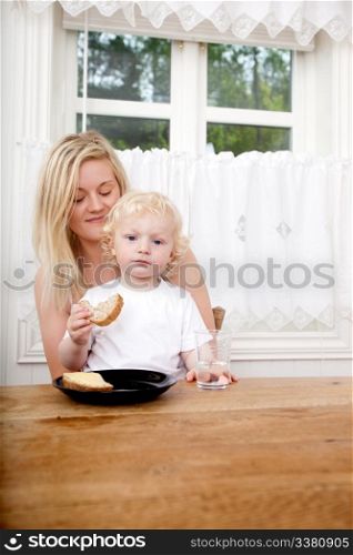 A young boy sitting on his mother&rsquo;s lap eating a sandwich