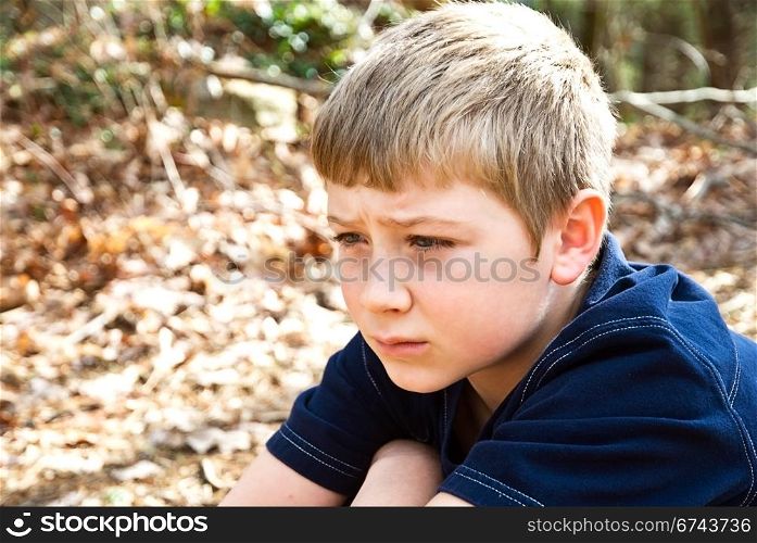 A young boy sitting outdoors, maybe he?s thinking, not feeling well, or lost, the expression could relate to many emotions.