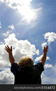 A young boy, with outstretched arms trying to reach for the sun