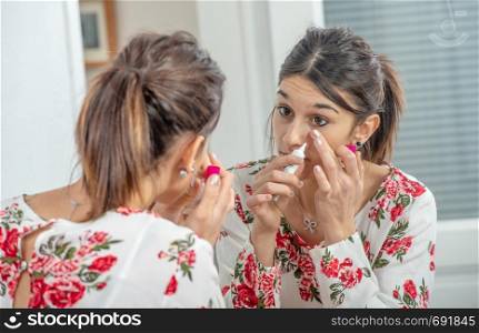 a young brunette woman putting makeup in the mirror