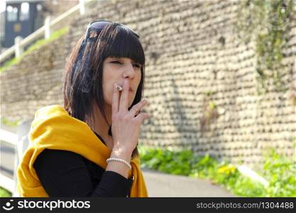 a young brunette woman smoking cigarette outside