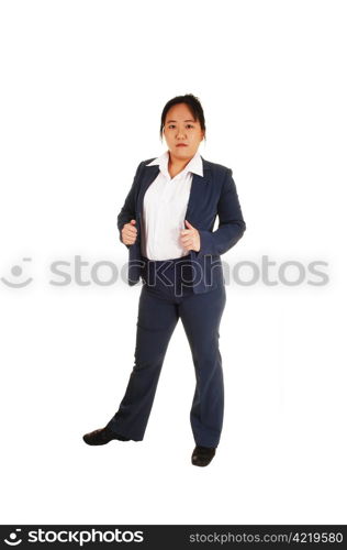 A young business woman in a blue suit and white shirt stands in thestudio for white background, looking into the camera.