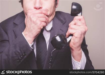 A young businessman is on the phone and covering his mouth in shock