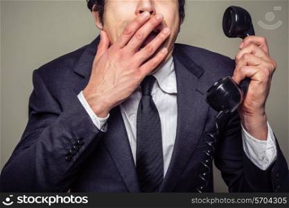 A young businessman is on the phone and covering his mouth in shock