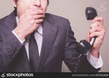 A young businessman is on the phone and covering his mouth in shock