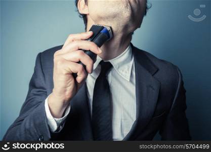 A young businessman is shaving with an electric razor