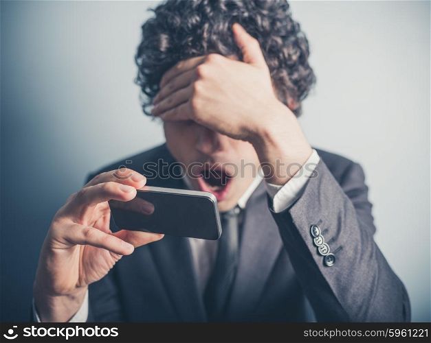 A young businessman is shocked by something on his smartphone