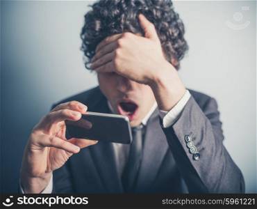 A young businessman is shocked by something on his smartphone
