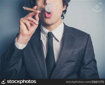 A young businessman is smoking a cigar and is blowing smoke rings