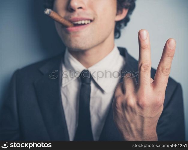A young businessman is smoking a cigar and is displaying a rude gesture