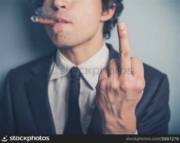A young businessman is smoking a cigar and is displaying a rude gesture