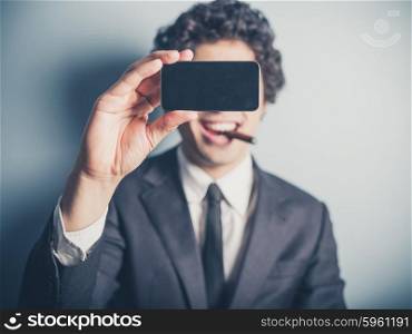A young businessman is smoking a cigar and is taking a selfie using his smartphone