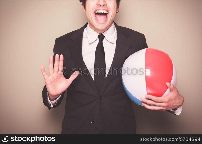 A young businessman is standing and holding a beach ball