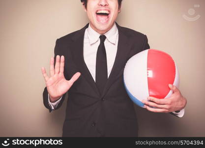 A young businessman is standing and holding a beach ball