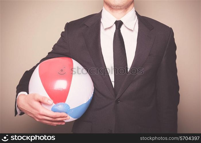 A young businessman is standing and holding a beach ball