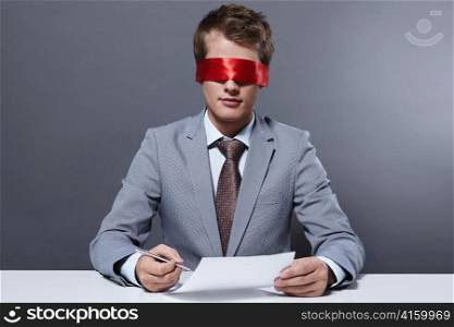 A young businessman signs a contract with a blindfold
