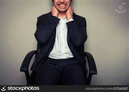A young businessman sitting in an office chair is having neck pains