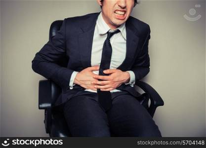 A young businessman sitting in an office chair is having stomach pains