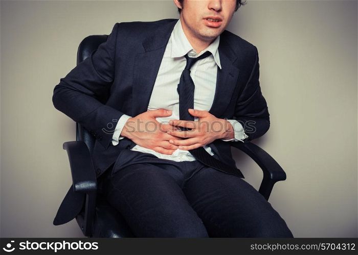 A young businessman sitting in an office chair is having stomach pains