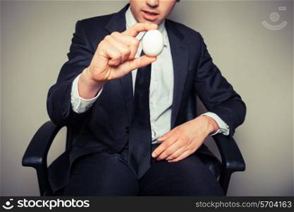 A young businessman sitting in an office chair is holding a boiled egg