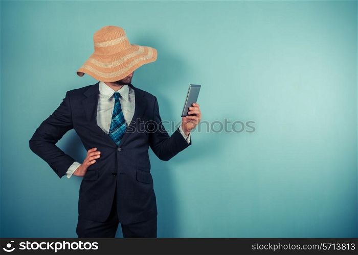 A young businessman wearing a large beach hat is reading on a tablet