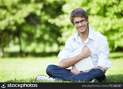A young businessman with a laptop on the grass