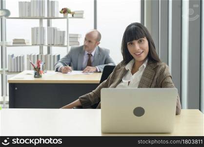 A young businesswoman sitting and working with laptop at modern office with colleague behind. Young businesswoman sitting and working with laptop at modern office with colleague behind