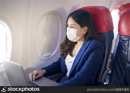 A young businesswoman wearing face mask is using laptop onboard, New normal travel after covid-19 pandemic concept. A young businesswoman wearing face mask is using laptop onboard, New normal travel after covid-19 pandemic concept