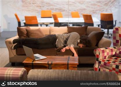 A young casual businessman sleeping on a sofa during a work break in a creative office