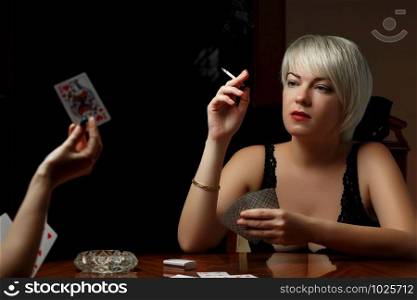 a young Caucasian blonde in black lingerie is sitting at a table and playing cards with another woman on undressing and Smoking cigarettes.