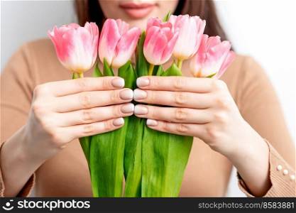 A young caucasian woman holds pink tulips in her hands against a white background. Young woman holds pink tulips